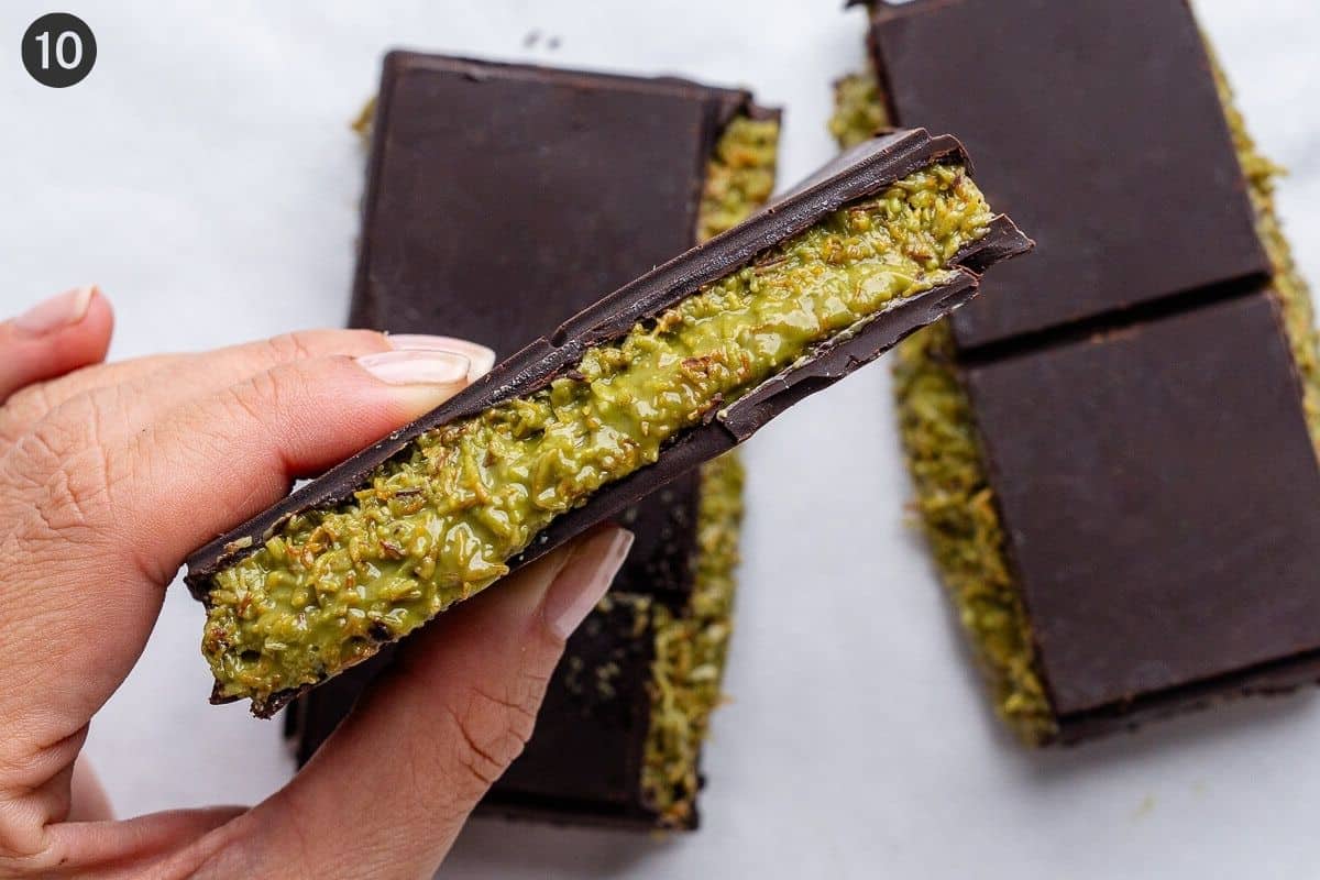Piece of chocolate held up to show the inside pistachio filling