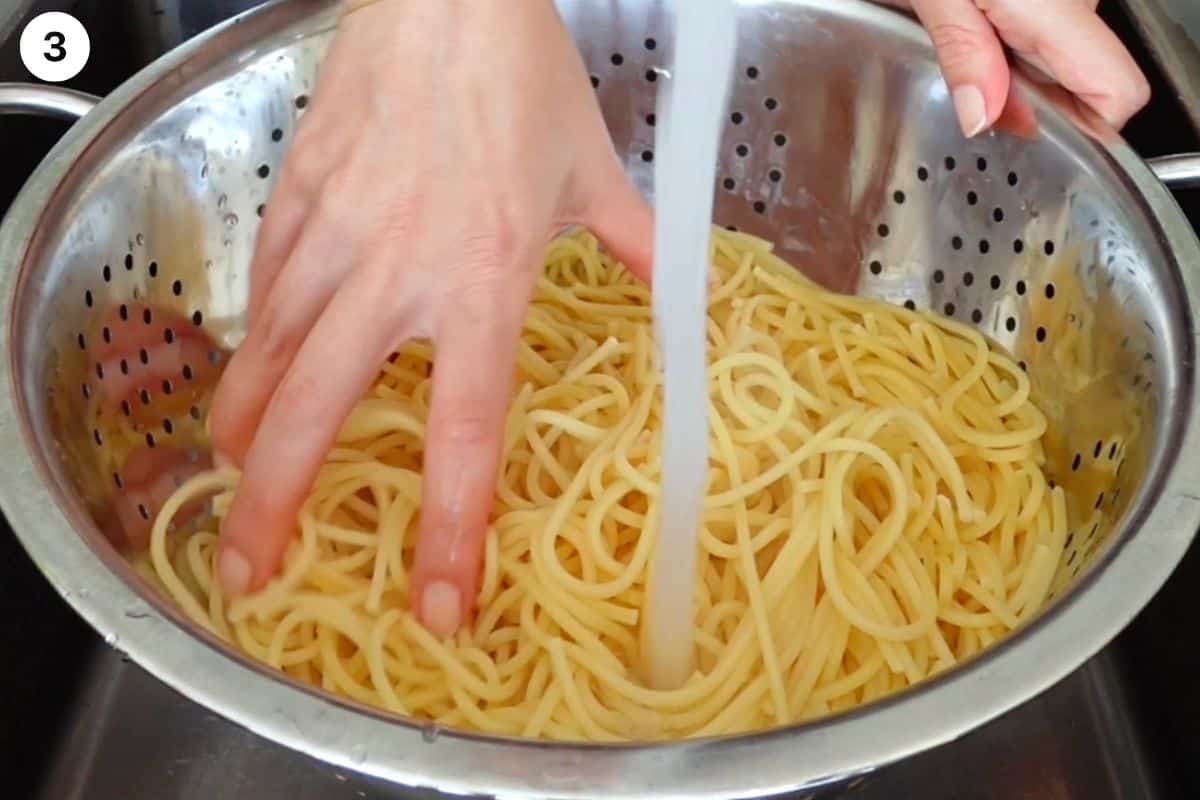 Pasta being rinsed under water in a colander