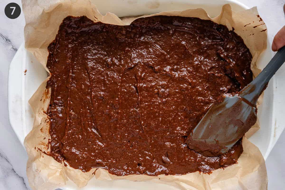 Brownie batter poured into a lined oven tray and top being smoothed
