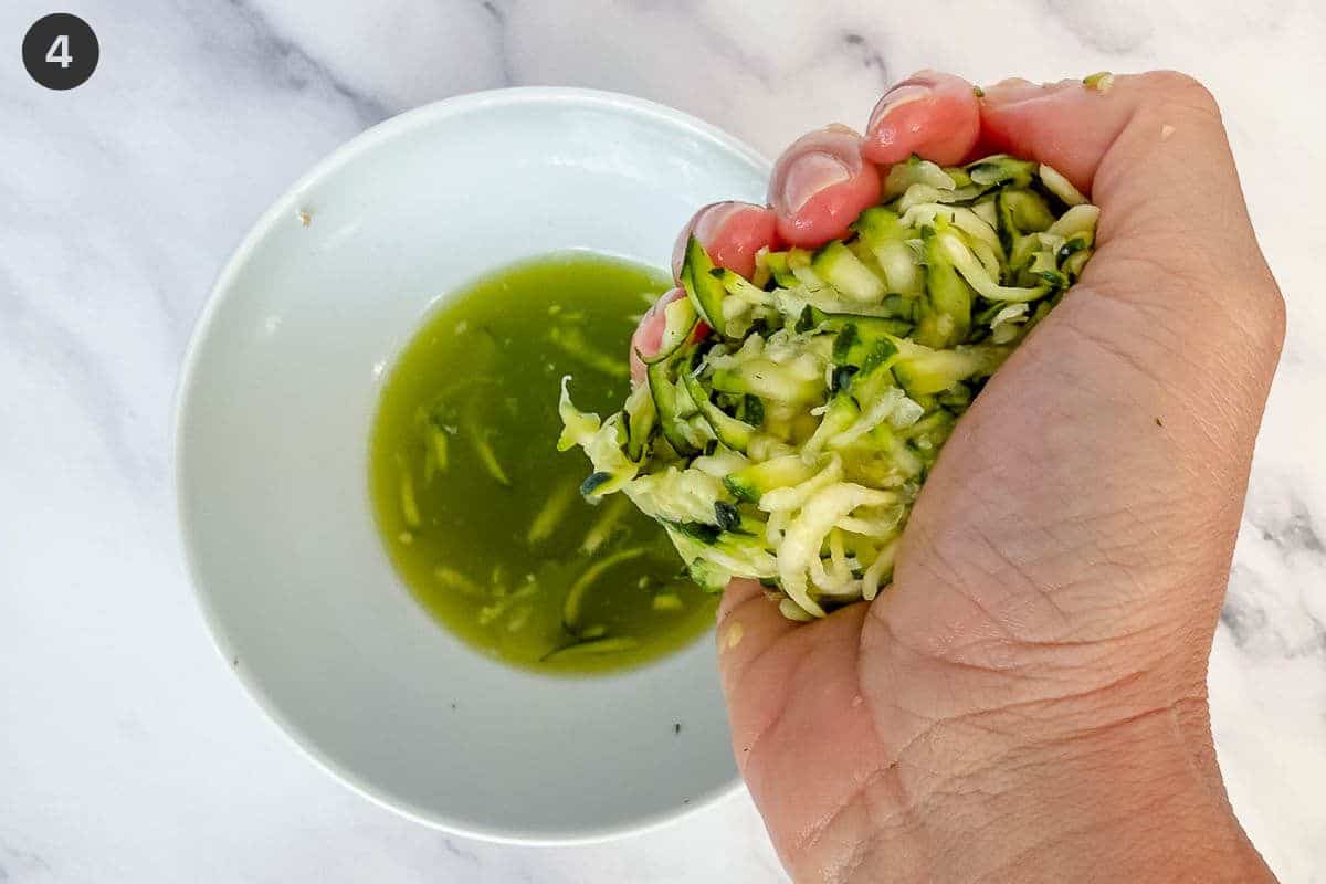 Grated zucchini being squeezed by hand to remove excess water