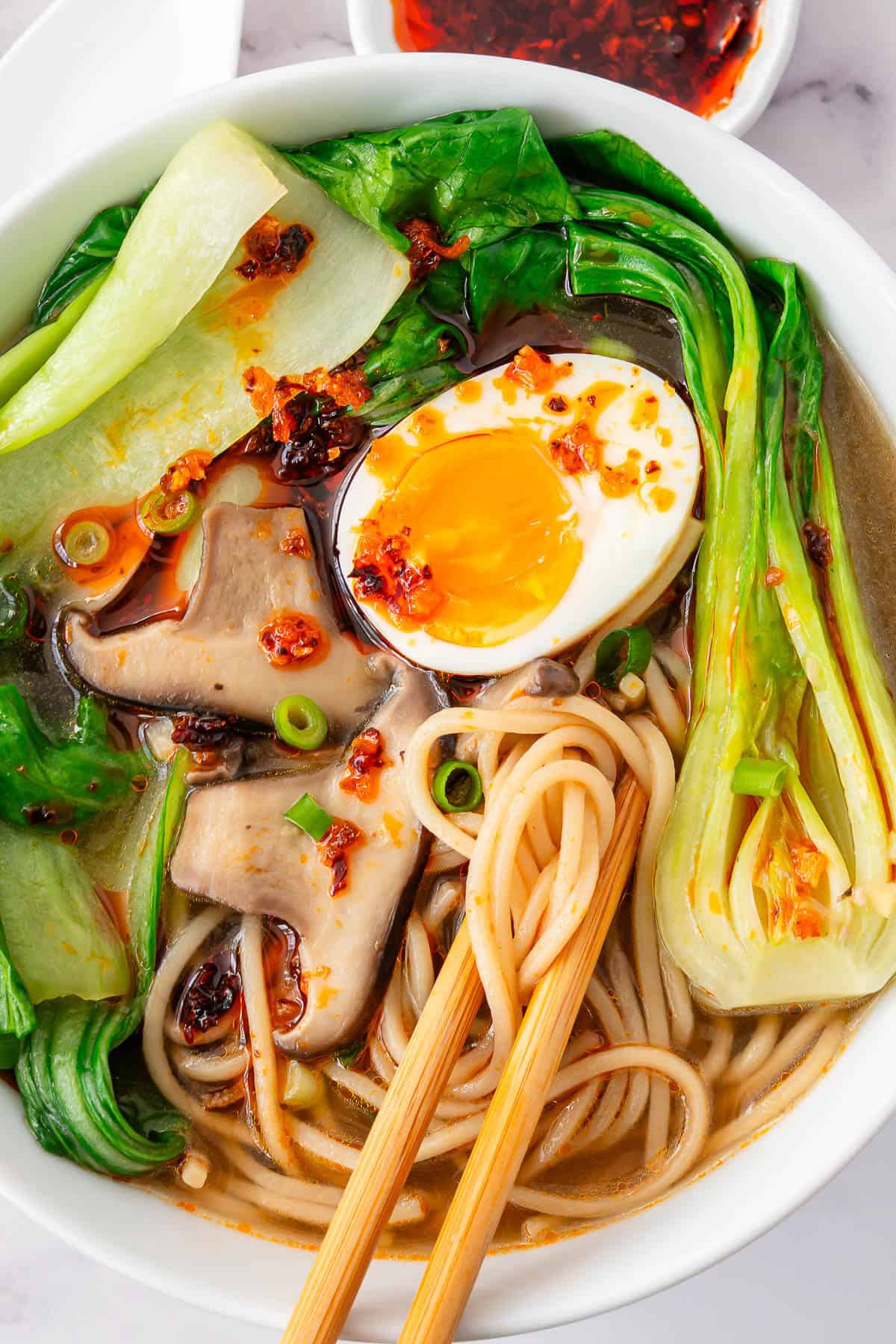 Chopsticks grabbing noodles in a bowl of boychoy soup