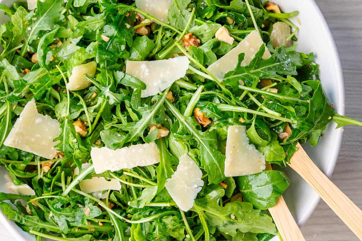 Close up of wooden spoons in a bowl of Arugula Salad