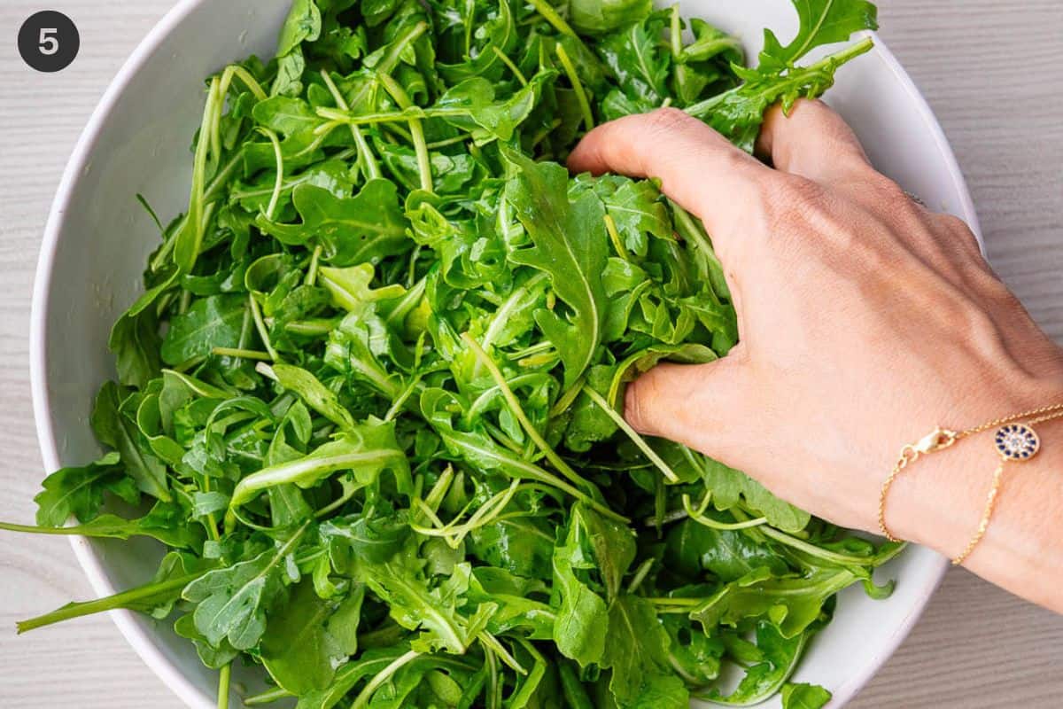 Dressing being mixed with arugula by hand