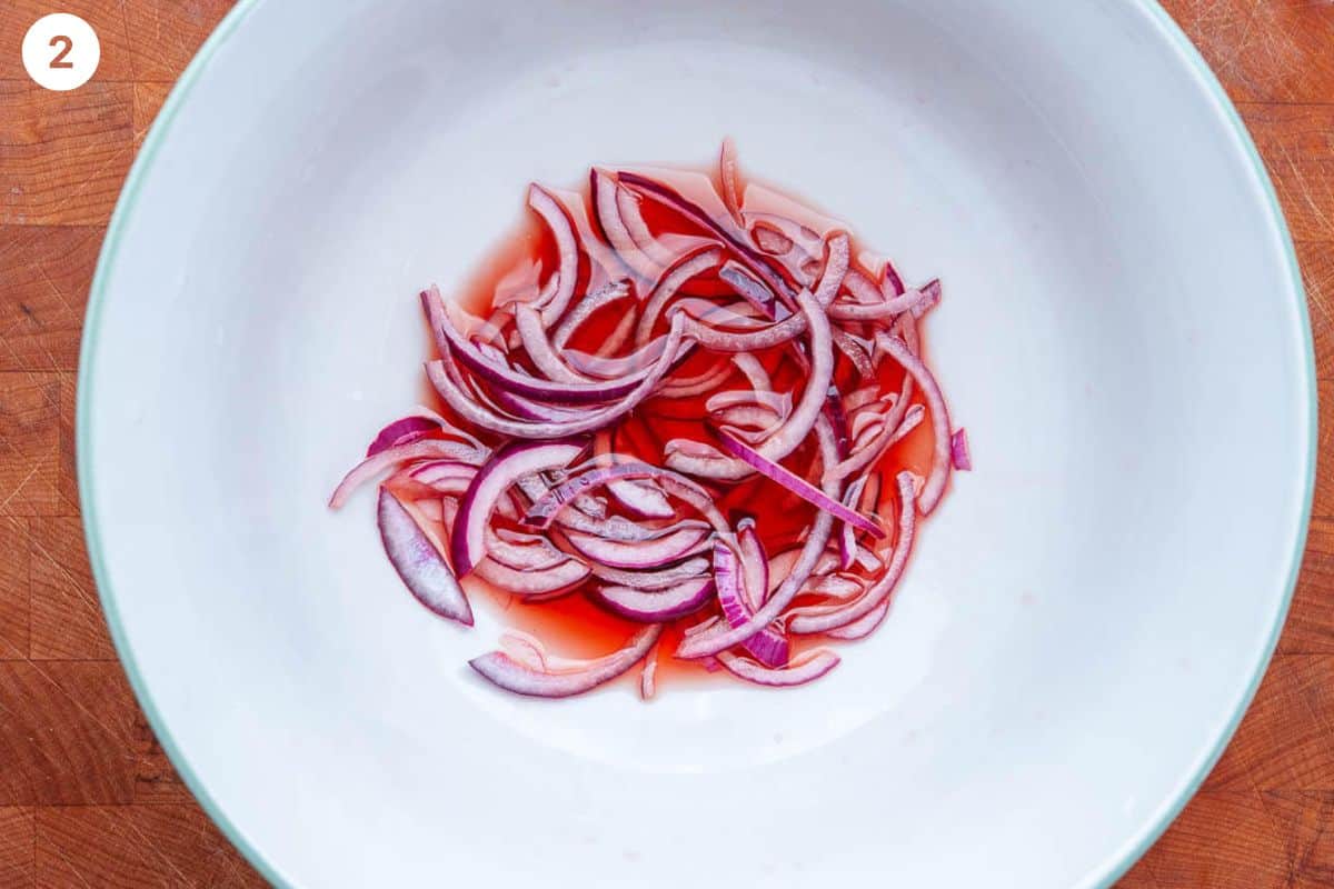 Sliced red onions being pickled in a large bowl