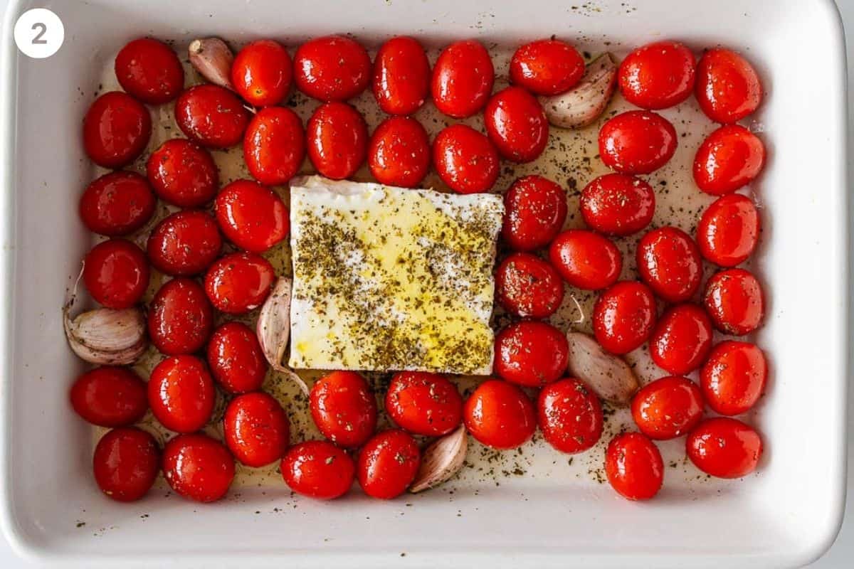 Feta cheese added to the middle of the baking dish with cherry tomatoes and garlic around it
