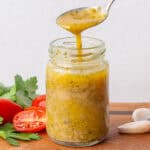Teaspoon full of Italian Dressing being poured into a small glass jar