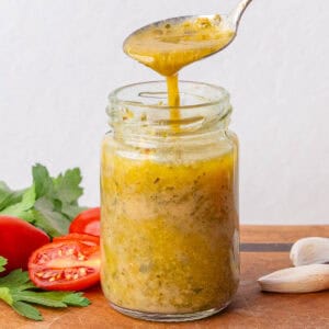 Teaspoon full of Italian Dressing being poured into a small glass jar