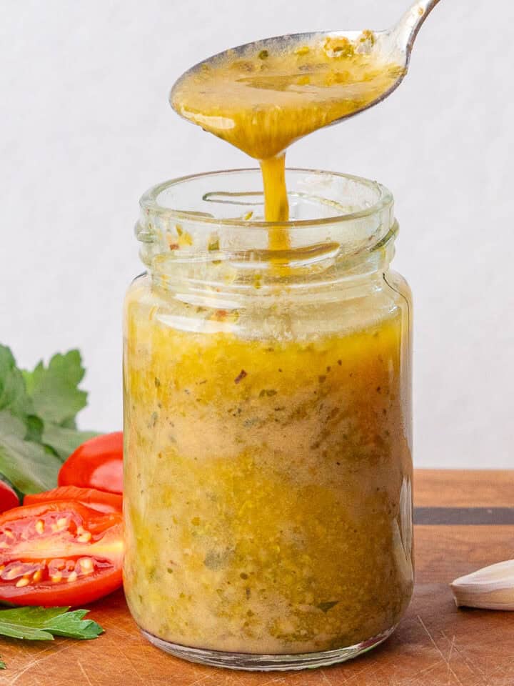 Teaspoon full of Italian Dressing being poured into a small glass jar
