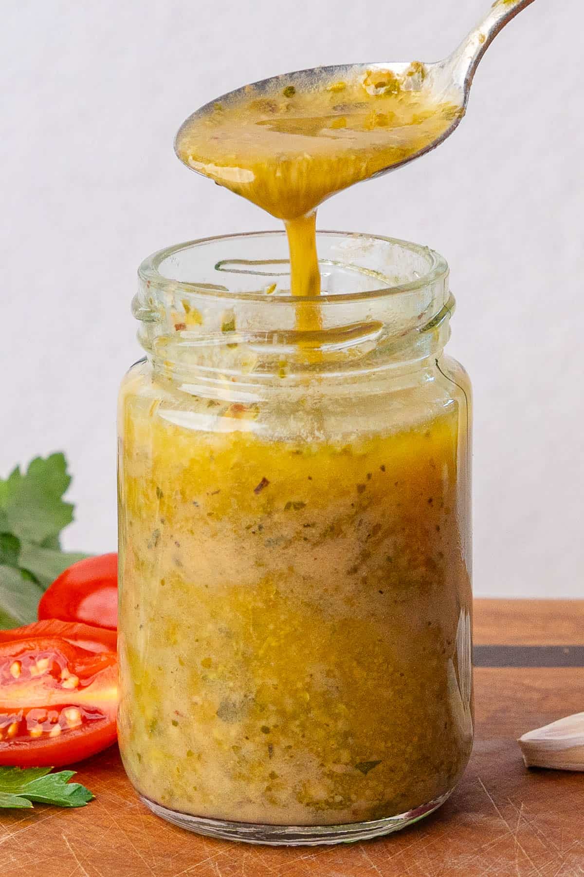 Spoon of Italian Dressing being poured into a small glass jar