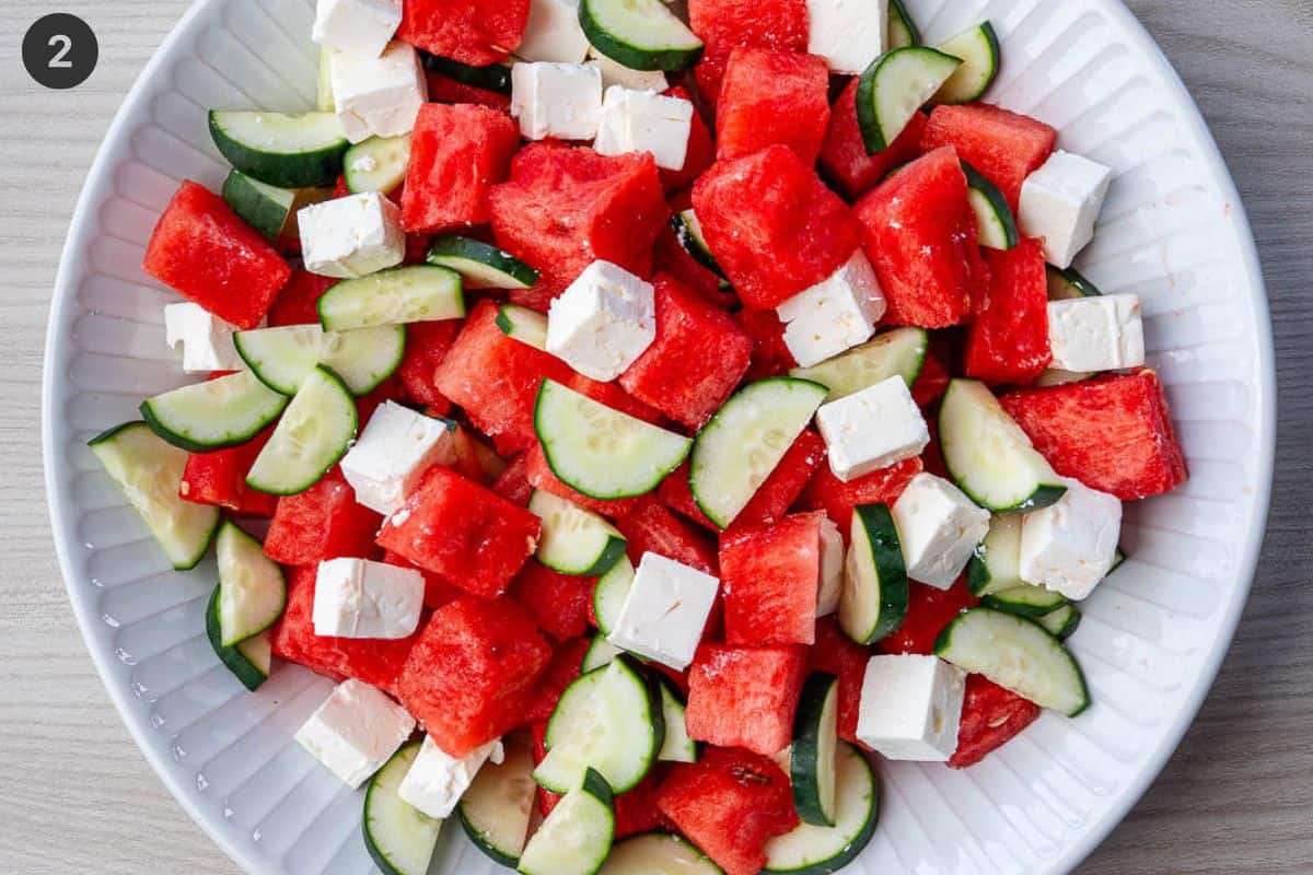 Cucumber and feta added to salad bowl with diced watermelon
