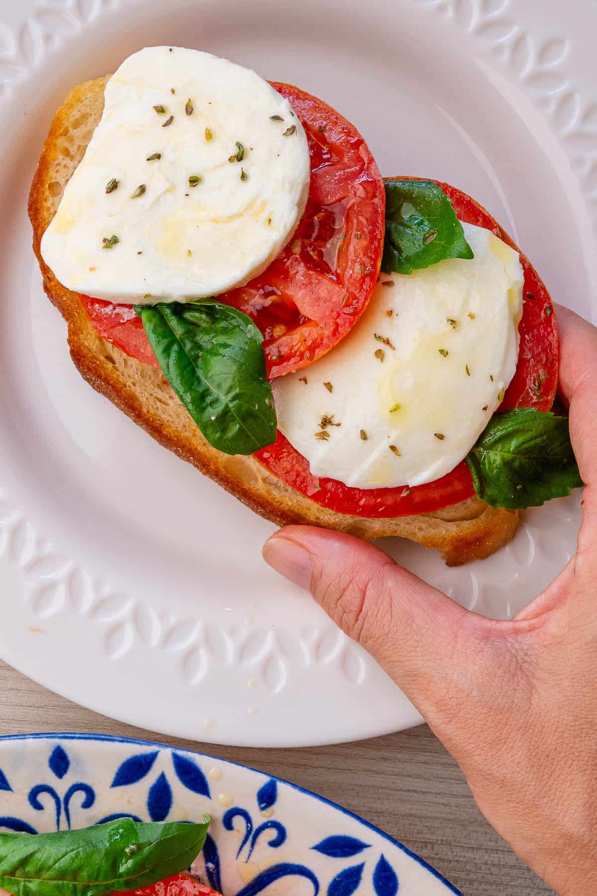 Toasted bread being picked up which is topped with caprese salad