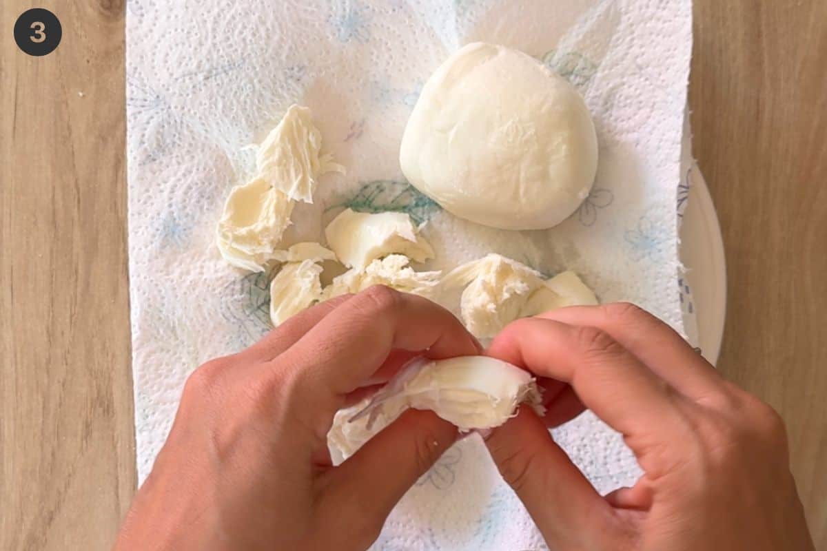 Fresh mozzarella being teared up and placed on paper towels