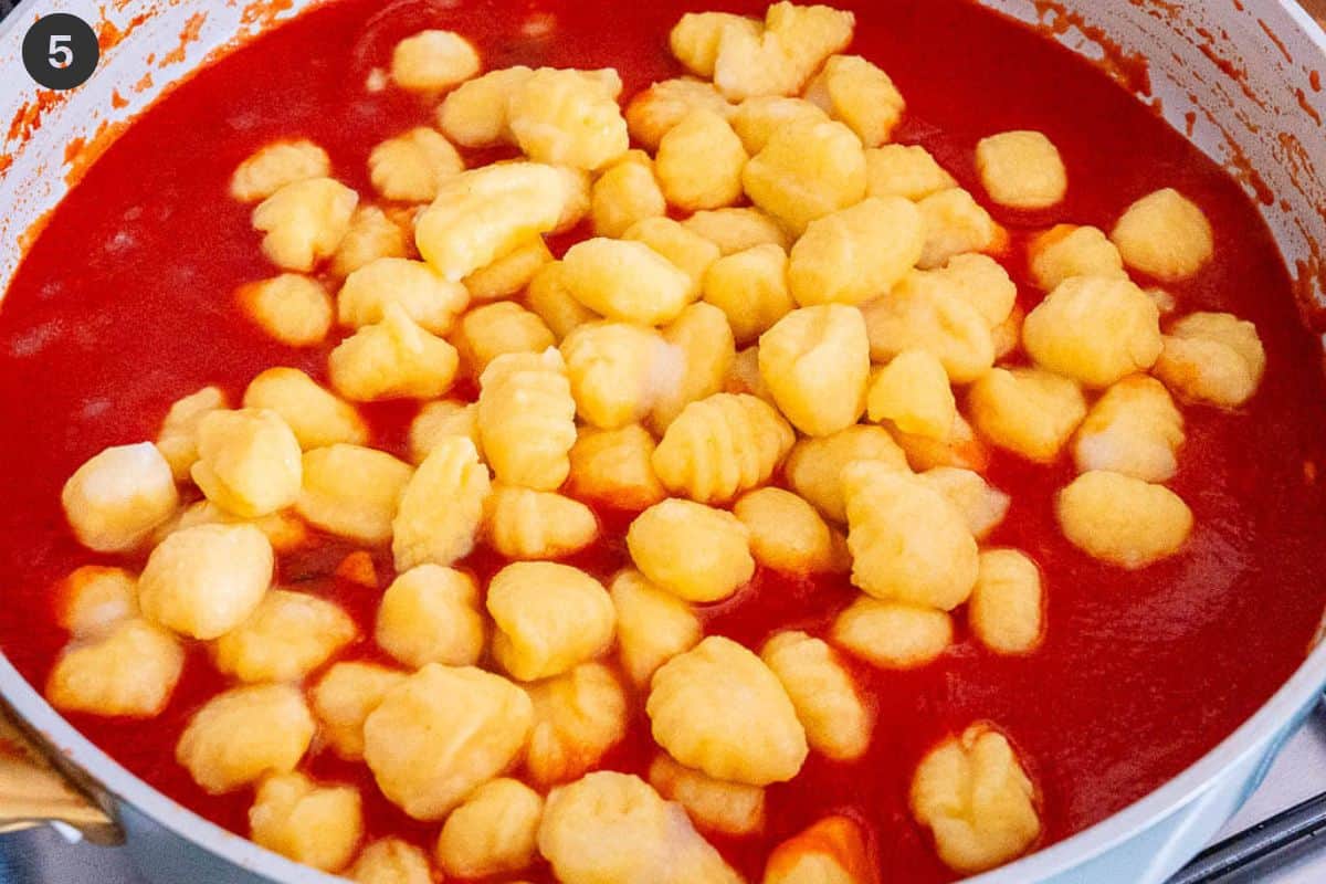 Cooked gnocchi added to tomato sauce in a pan