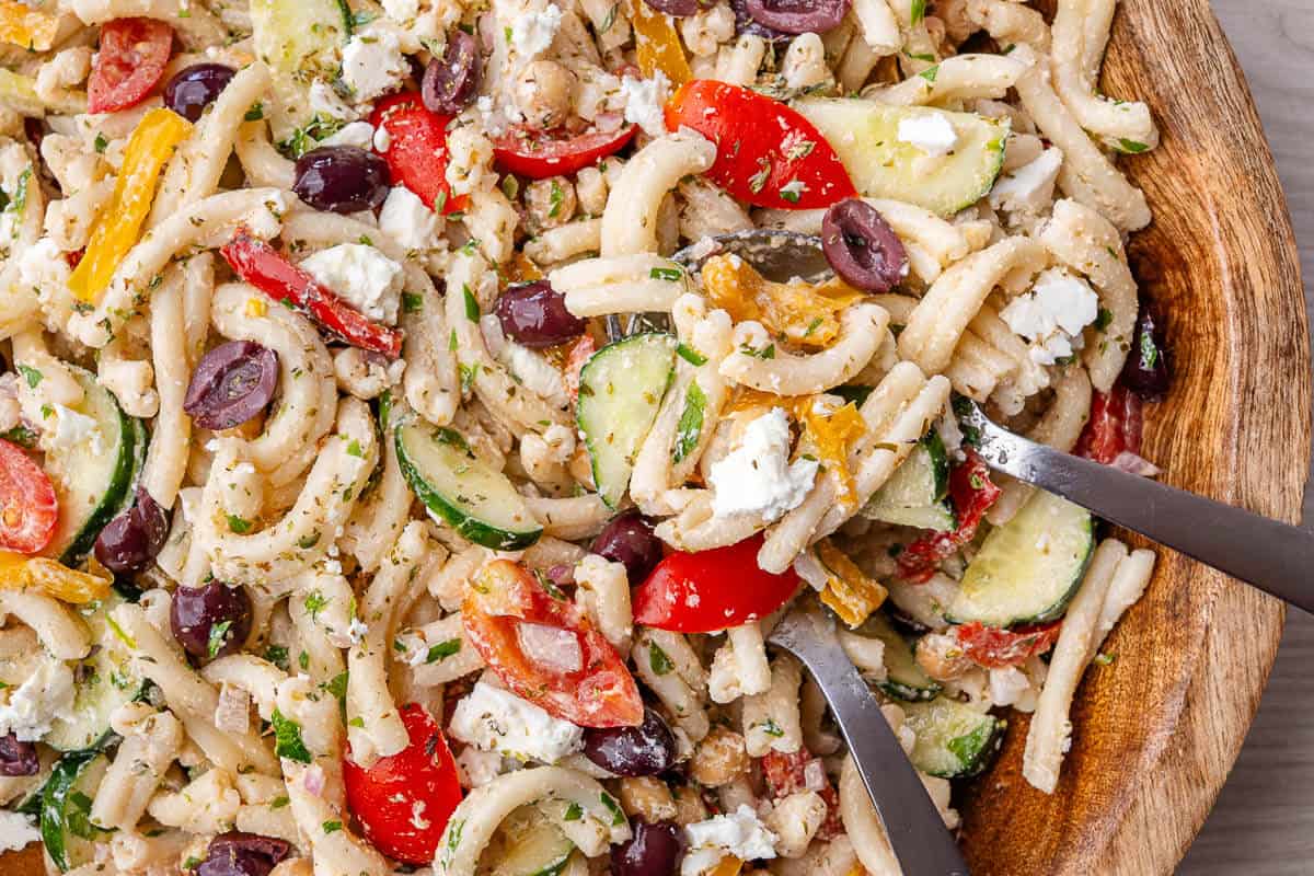 Fork and spoon in a large bowl of Greek Pasta Salad
