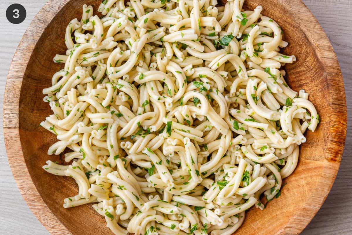 Cooked pasta added to large salad bowl with olive oil and parsely