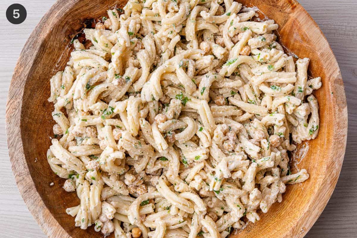 Feta dressing and chickpeas added to pasta in a large bowl