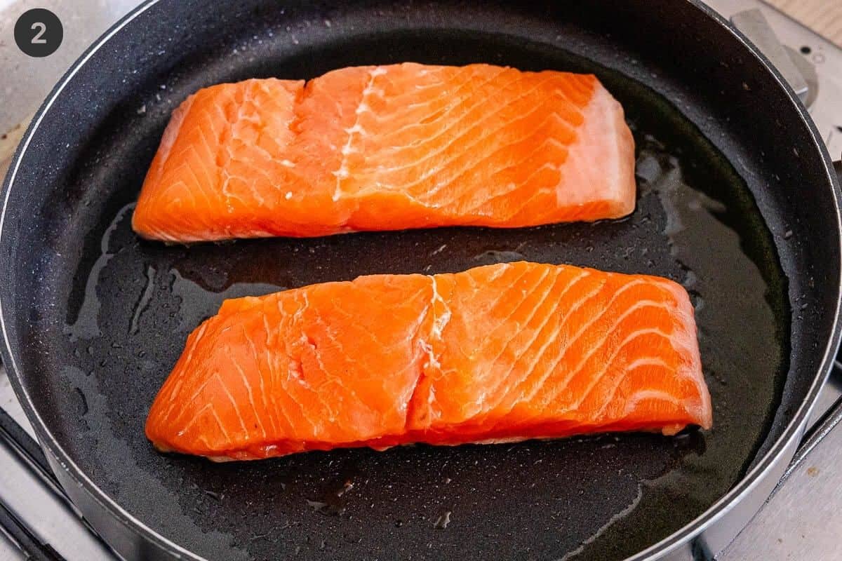 Two salmon fillets added to a pan with olive oil