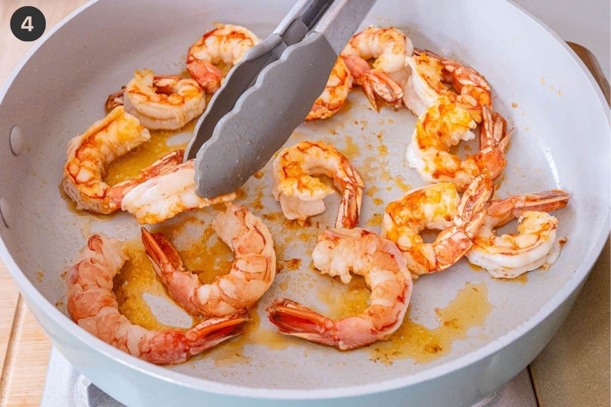 Shrimp being turned around to cook the other side with tongs