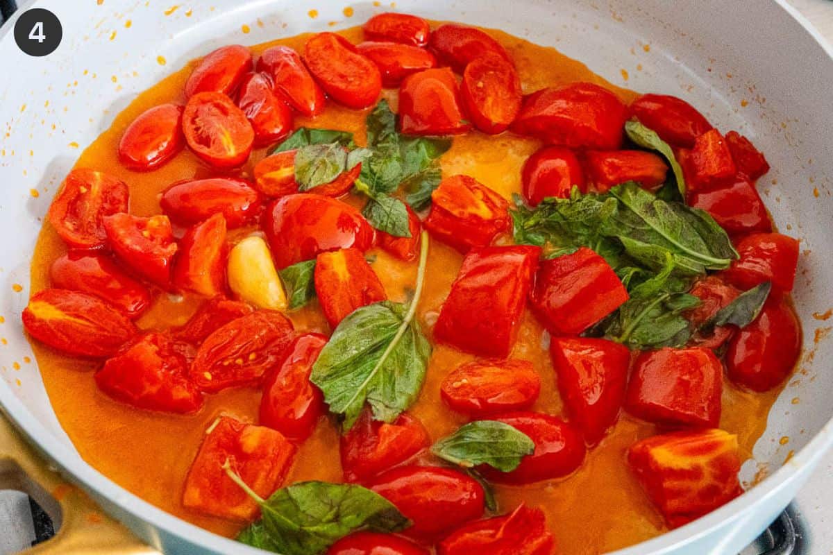 Basil and water added to tomatoes in a pan before simmering