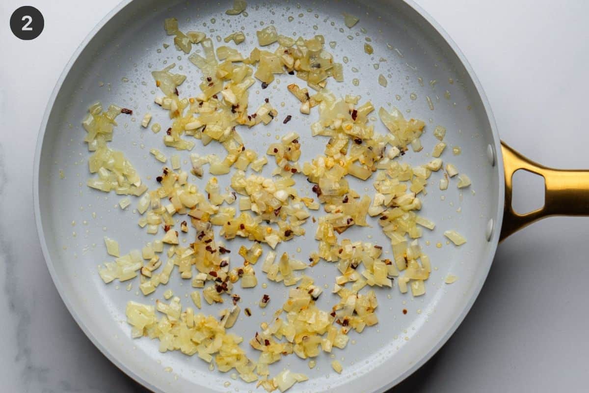 Onions and chili flakes being sautéed in a pan with olive oil
