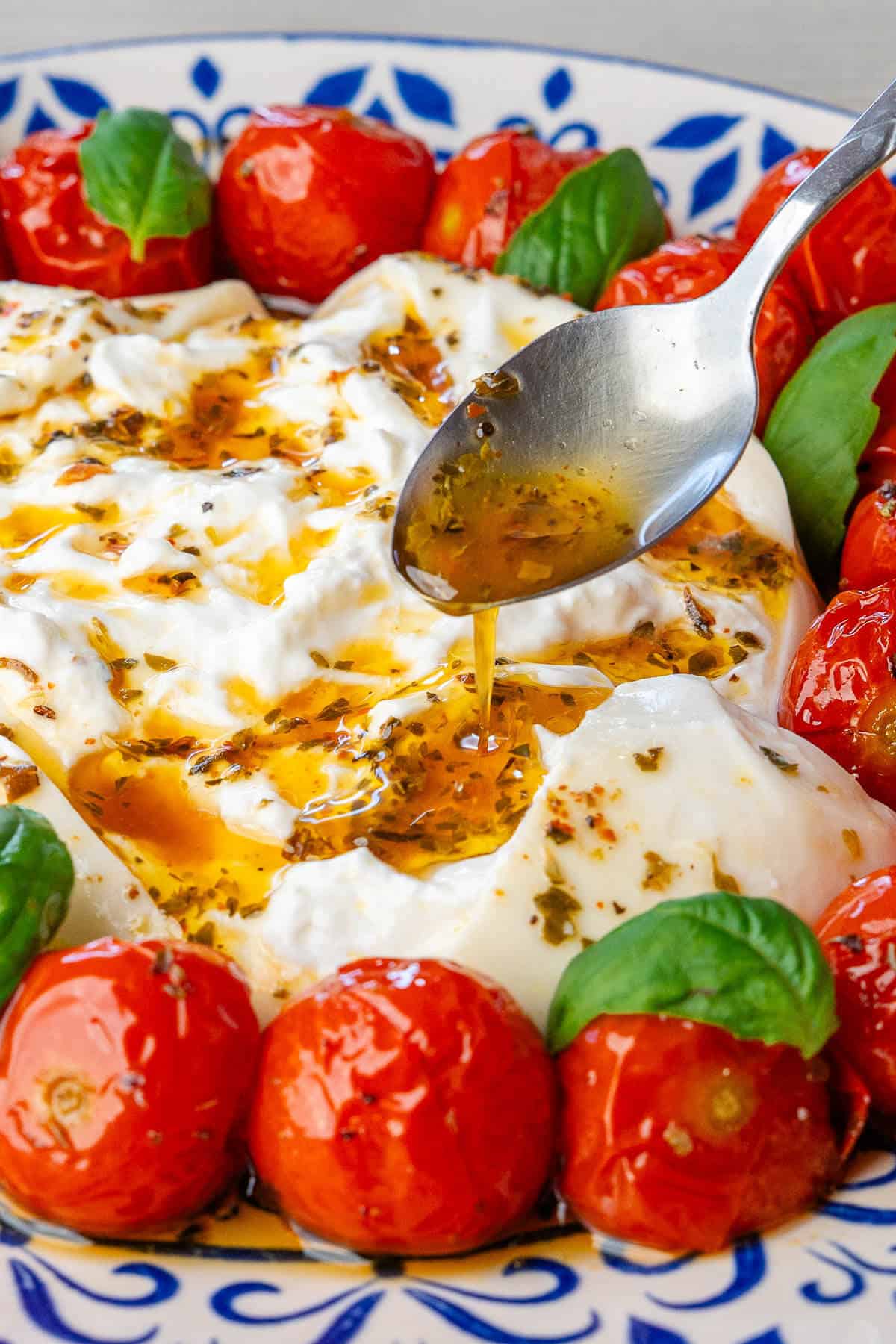 Spoon of dressing being poured on top of the burrata cheese