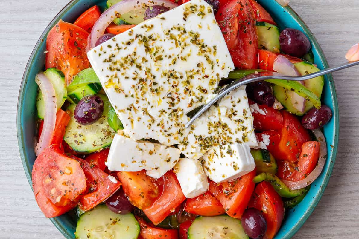 Fork breaking up feta cheese in a Greek Salad