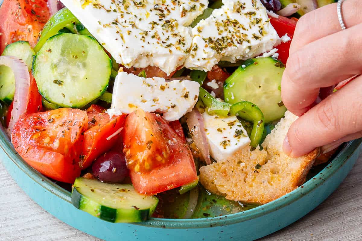Bread being dipped into the Greek Salad dressing at the bottom of the bowl