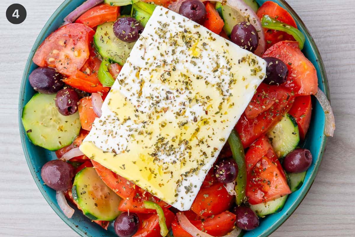 Salad arranged in a serving bowl with feta placed on top with oregano and olive oil