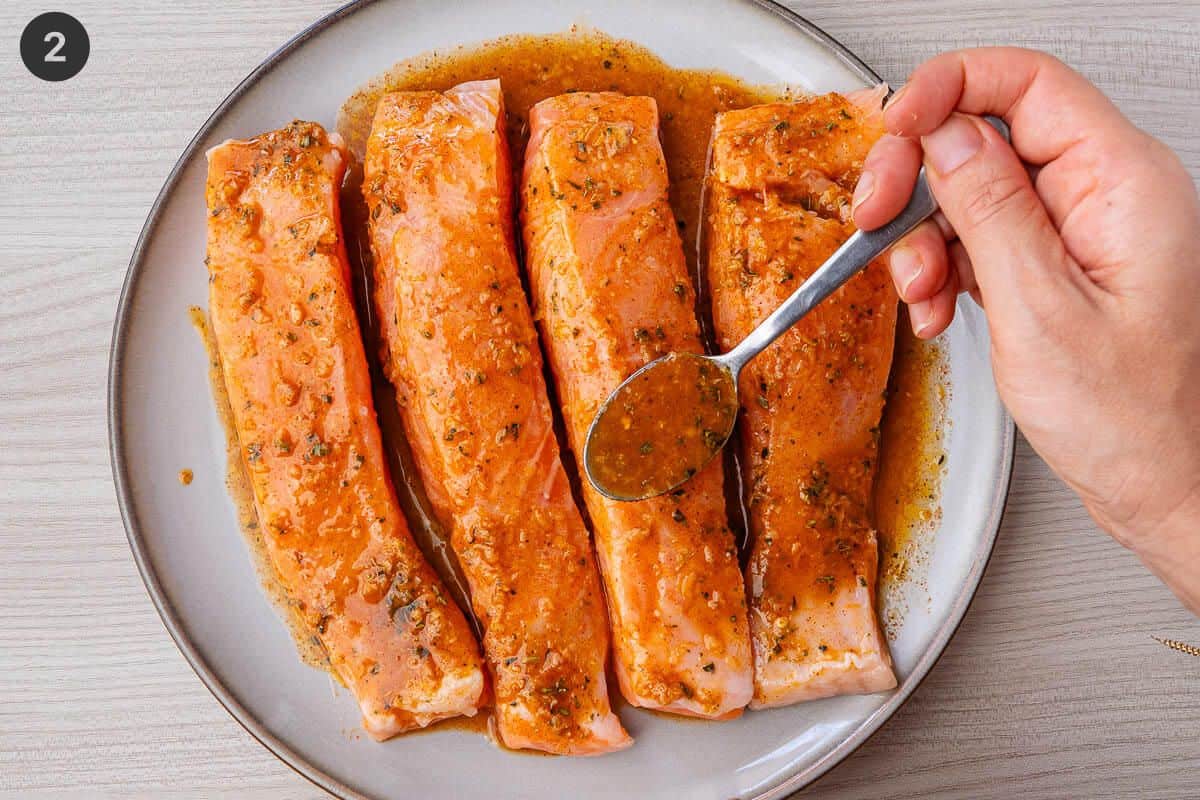 Lemon garlic marinade being spooned on top of salmon fillets