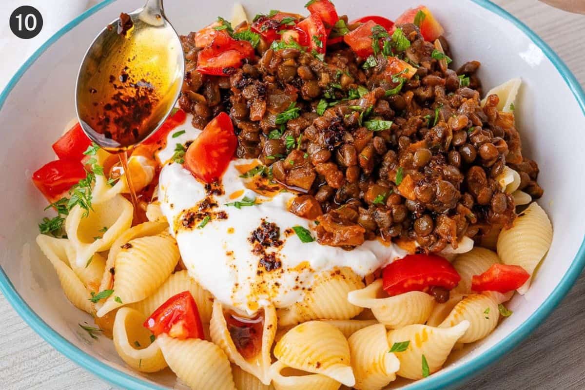 Final bowl served with pasta, yogurt sauce, lentil mixture, chopped tomatoes and aleppo pepper drizzled on top