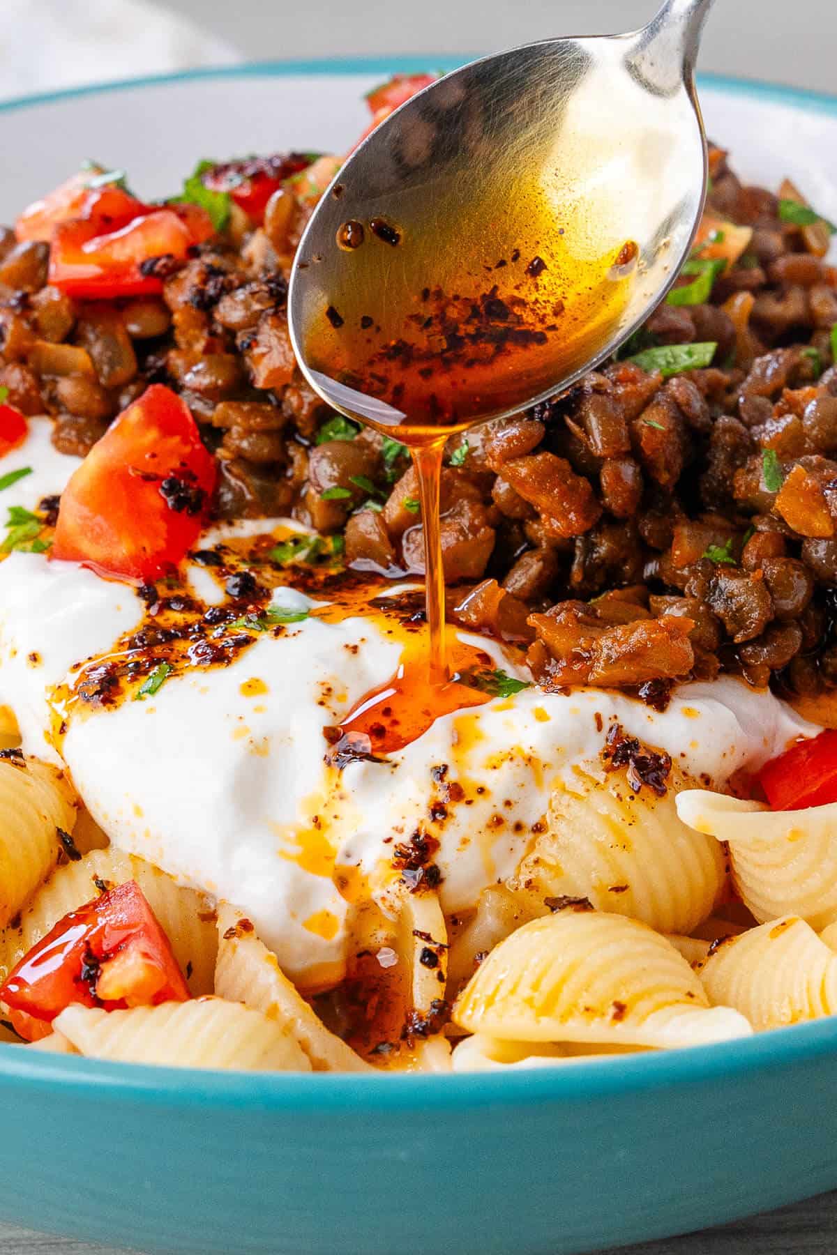 Close up of spoon pouring aleppo pepper over the Turkish Pasta